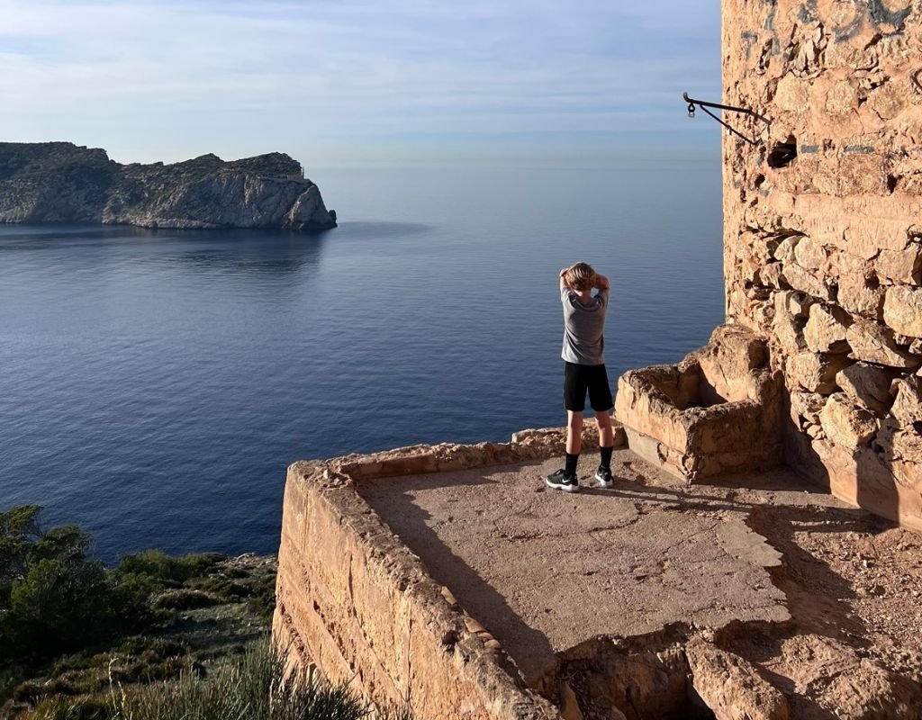 Colleen's youngest looking out at sea while standing on a cement platform in a bay of tranquil blue water. 