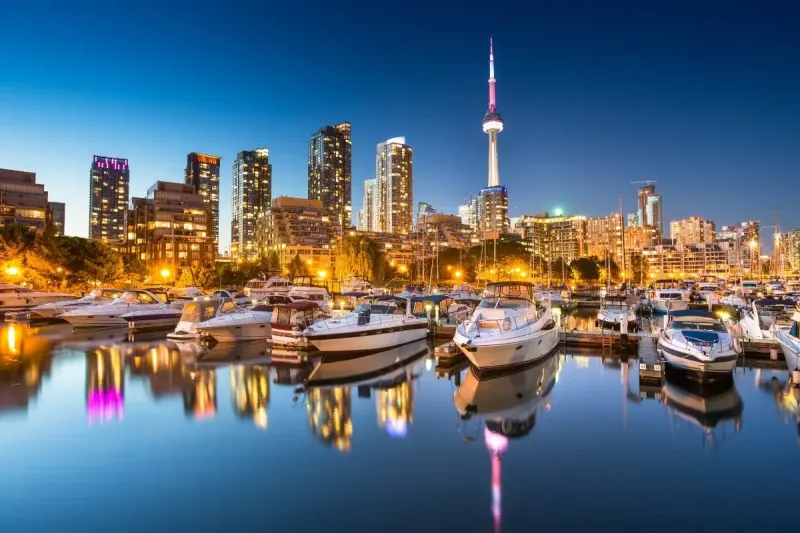 Boats parked in the marina in Toronto at dusk, in Toronto's downtown. The tall buildings are reflected in the water around the boats.