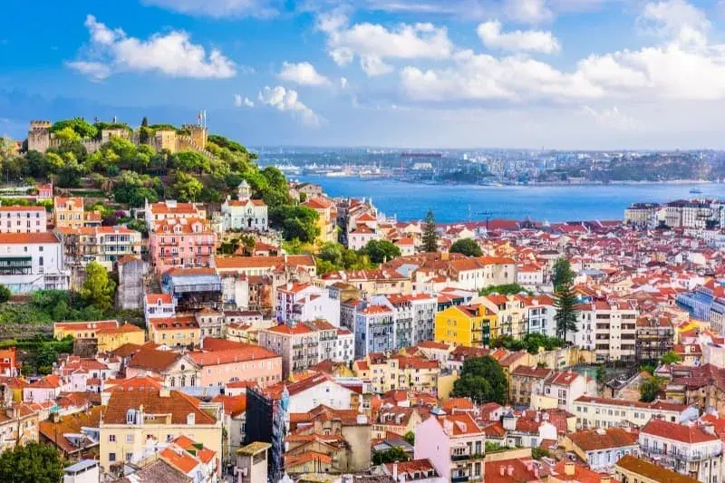 Lisbon's castle towering over the rest of the city, with the river Tejo in the background on a sunny day.