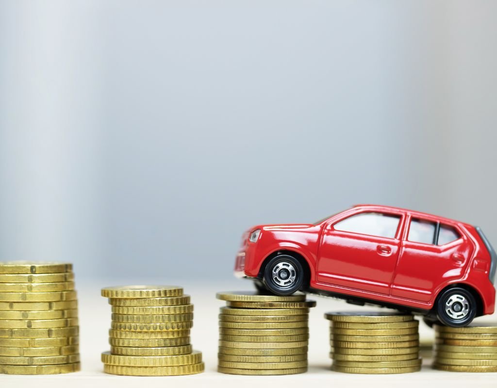 A miniature red car perched on stacks of coins, symbolizing financial planning. 