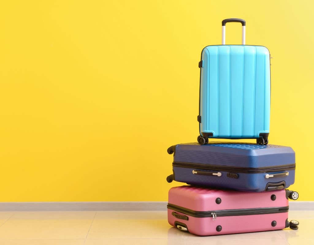 Three colourful suitcases piled on top of each other in front of a yellow wall.