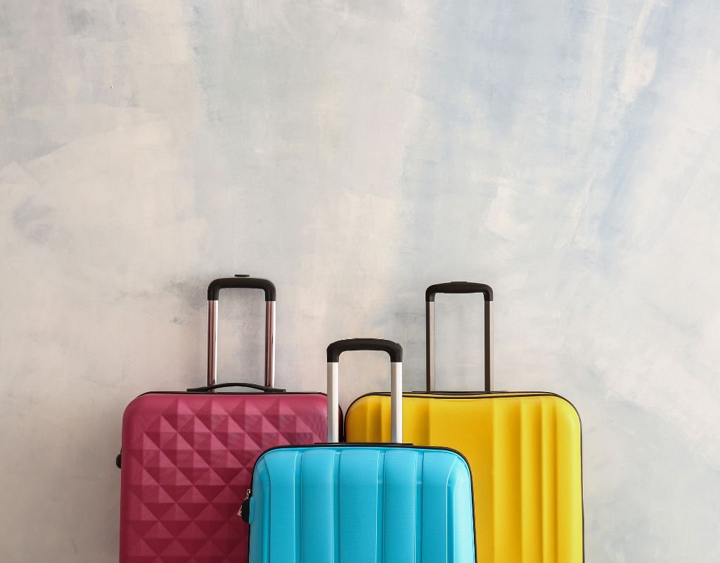 Three hard-shell suitcases in pink, blue, and yellow, standing upright against a light blue wall, ready for an international adventure.