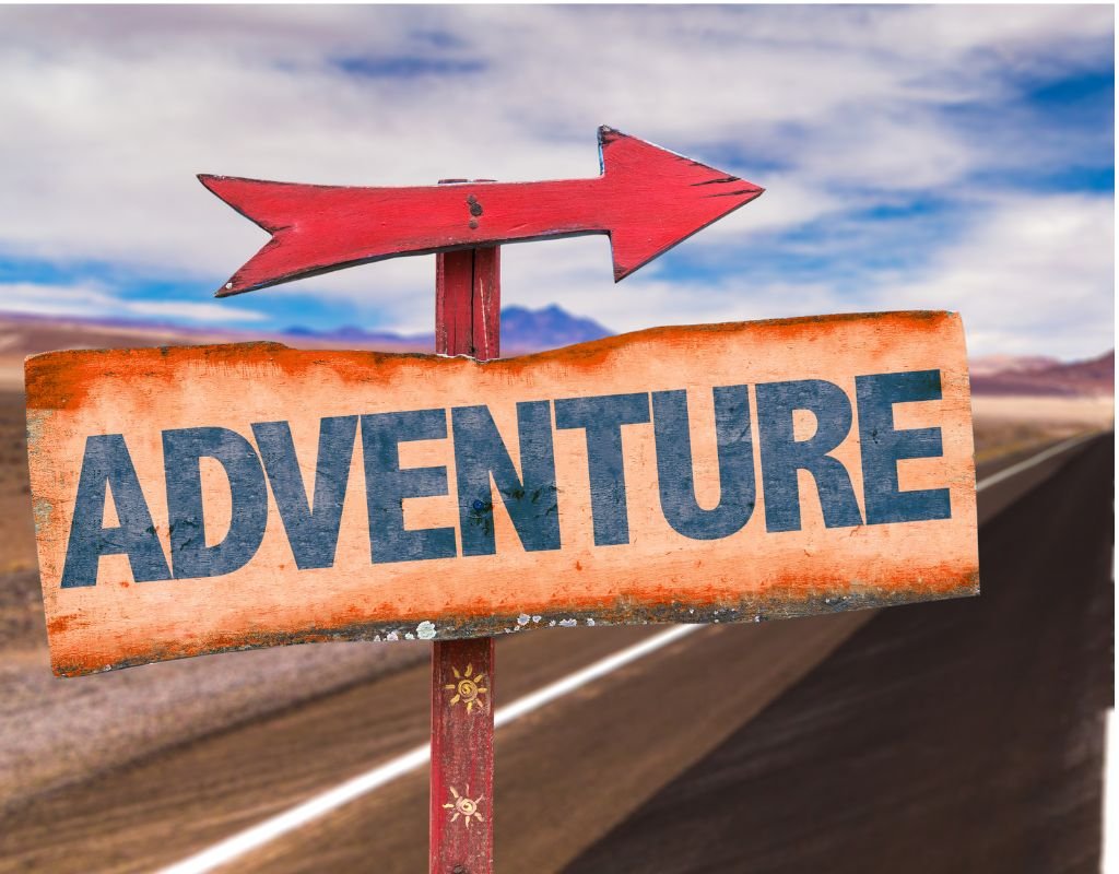 A rustic wooden sign with 'Adventure' written in bold letters points down an open road in a desert landscape. The best countries for expats often promise adventure, cultural immersion, and new beginnings.