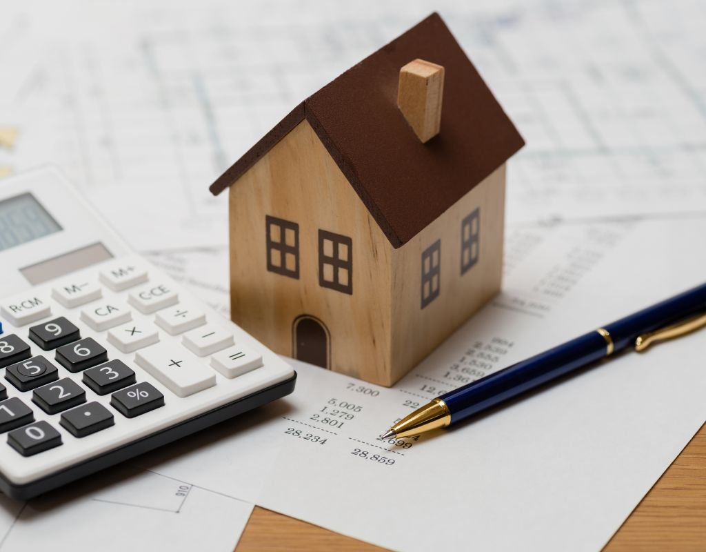 A small wooden house sits next to a calculator and pen on top of financial documents, representing real estate planning. For expats, considering the best countries to relocate to often involves understanding property laws and financial planning.