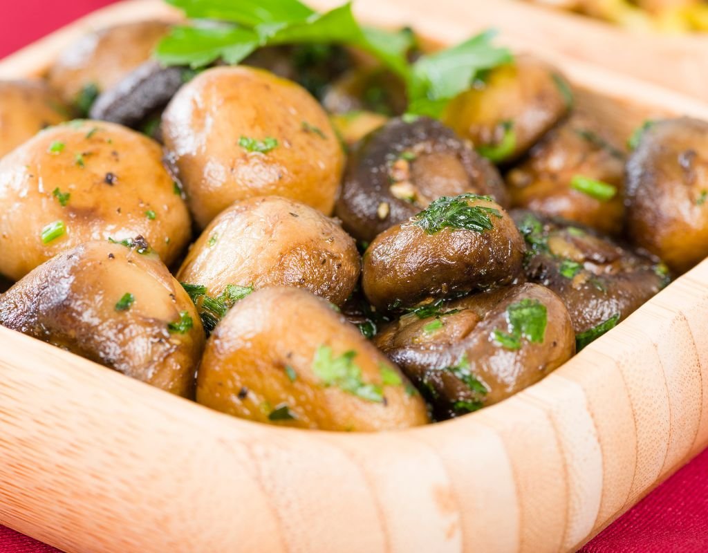 A wooden dish filled with garlic sautéed mushrooms, glistening with olive oil and garnished with fresh parsley—an earthy and flavorful Spanish tapa.