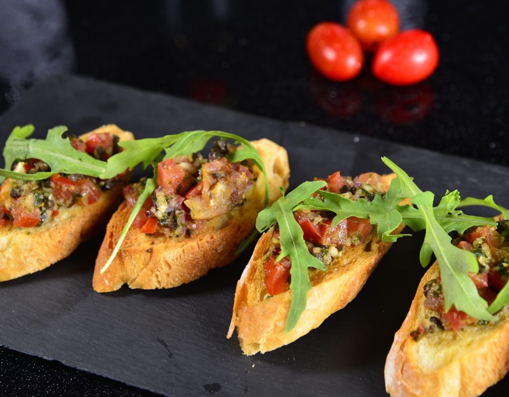 A plate of tosta de escalivada, featuring toasted bread topped with roasted peppers, eggplant, and tomatoes, finished with arugula and olive oil. A delicious and colorful example of vegetarian dishes in Spain.