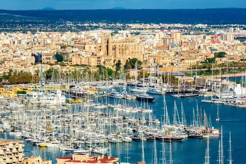 Mallorca is one of the best places to live in Spain by the sea. The Main Marina in the foreground with all its white sail boat masts and the cathedral and city center in the background.