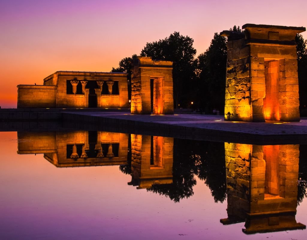 The Temple of Debod, an ancient Egyptian monument in Madrid, beautifully illuminated at sunset, with its reflection shimmering in the still water. Is Madrid worth visiting? This breathtaking historical site proves that it is.