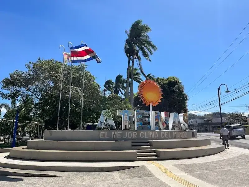 The Atenas sign at the entrance of the city, as seen on a sunny day with trees in the background.