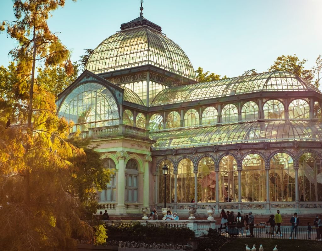 The stunning Palacio de Cristal, or Glass Palace, in Madrid’s Retiro Park, bathed in warm golden light as visitors admire its intricate glass and iron architecture. Is Madrid worth visiting? This enchanting landmark makes a strong case for it.