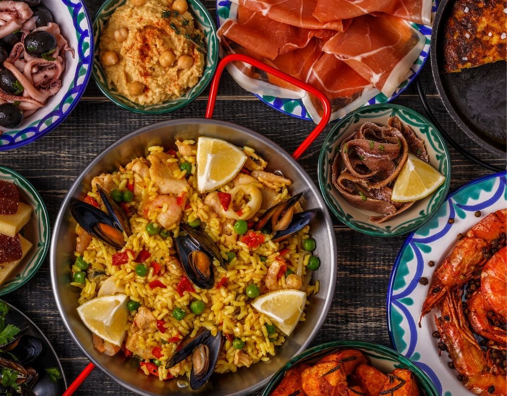 A mouthwatering spread of Spanish cuisine, featuring a pan of seafood paella with mussels and shrimp, surrounded by tapas like jamón ibérico, olives, and grilled octopus.