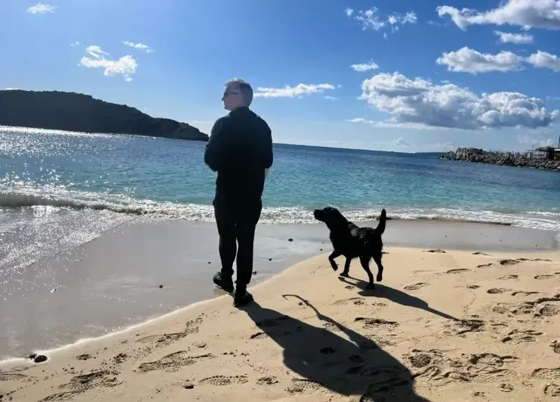 Shipping your pet internationally is a long process which can be quite stressful. Man with black dog on the beach on a sunny day in Spain.