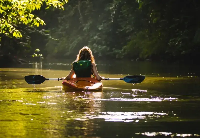 A blond woman seen from the back  kayaking in a sea kayak on shallow water along the murkey waters of Drake Bay.