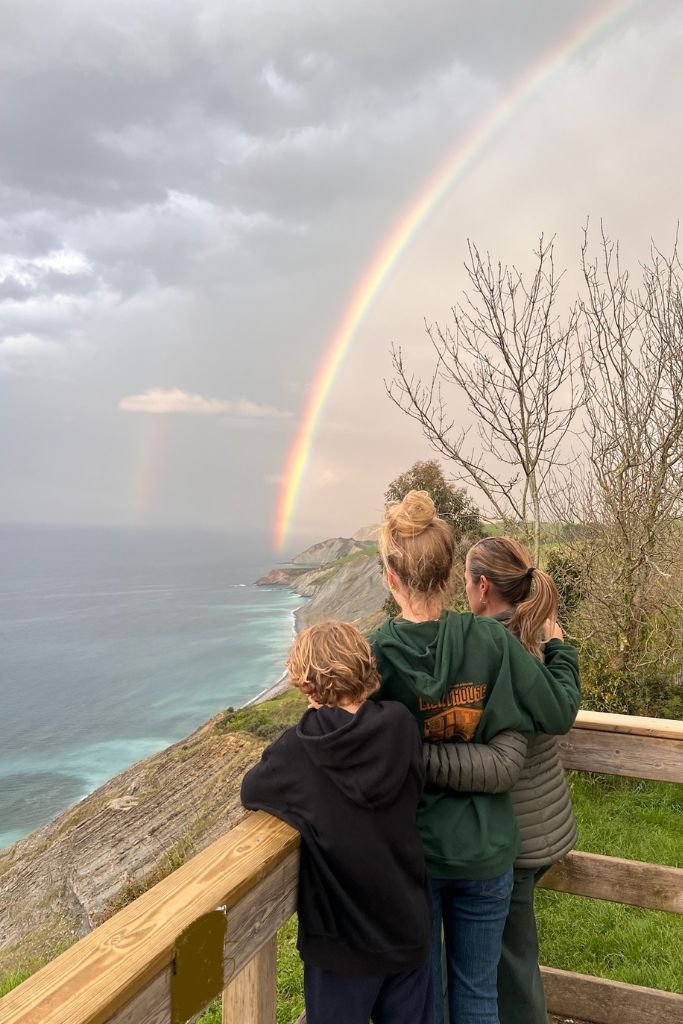 Woman and her two children  looking at a rainbow above the ocean on the coast of Spain Spain in considered one of the best countries for expats.