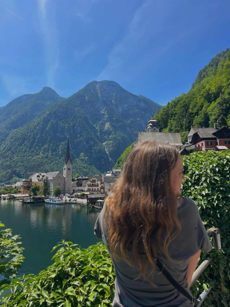 A woman standing in front of the majestic mountains and buildings in Halstatt.