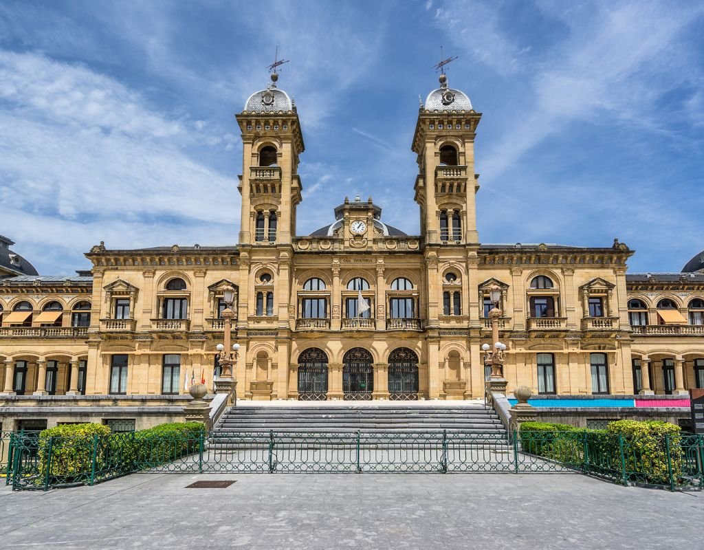 The grand façade of San Sebastian’s City Hall, a historic building with two towers and intricate architectural details, standing under a bright blue sky. An iconic landmark in the heart of the city.