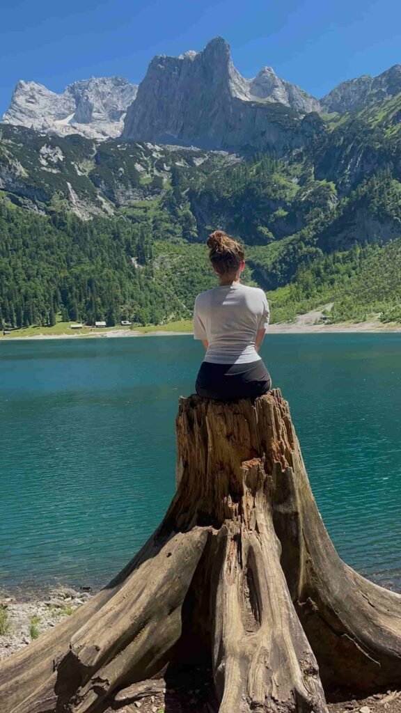 A woman facing the lake sitting on a trunk.