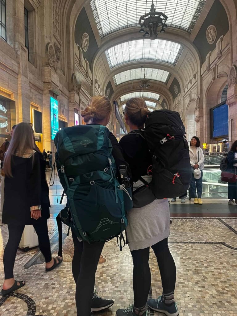 Two back packers looking down towards the end of the he Milan Train Station filled with people.