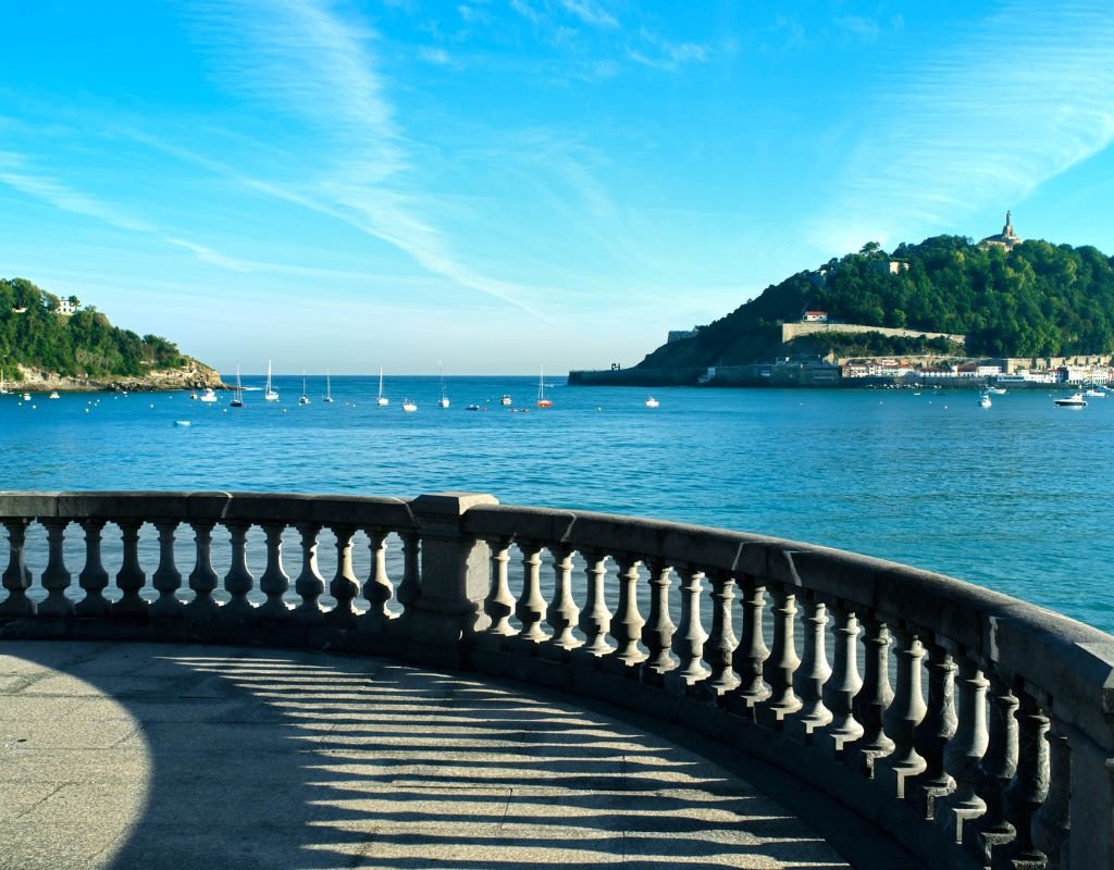 A curved stone balustrade overlooking the sparkling blue sea of San Sebastian, with sailboats floating near the coastline. A peaceful spot to admire the city’s coastal beauty.