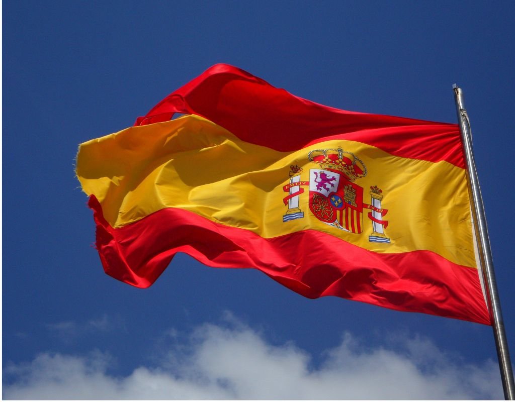 The Spanish flag billows against a clear blue sky, its coat of arms symbolizing Spain’s heritage. How to get Spanish citizenship? Begin with legal residency and embrace the country’s vibrant traditions.