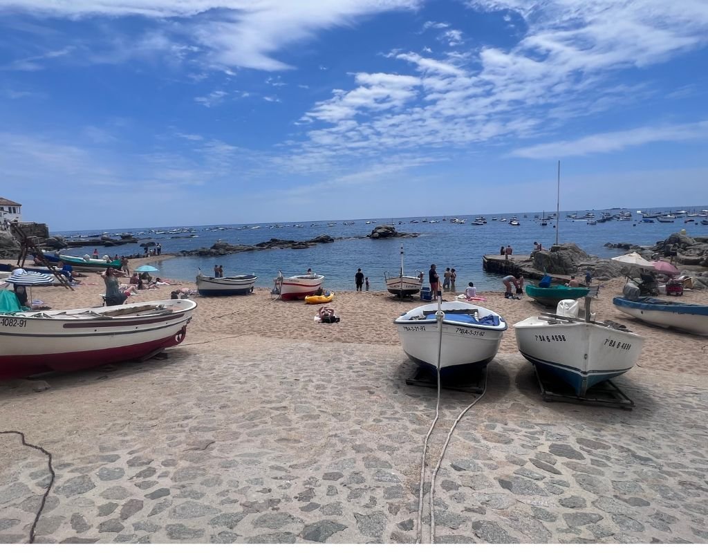 A scenic beach with colorful fishing boats resting on the sand and people relaxing under the sun, representing Spain’s coastal charm.