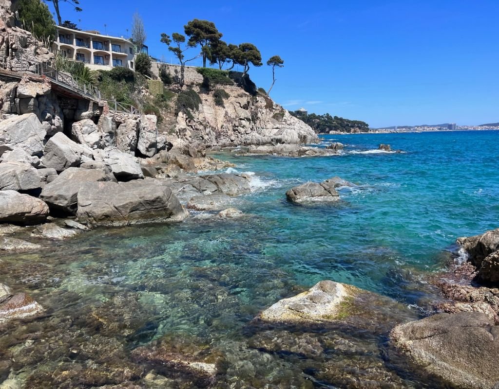 A rugged shoreline with vivid turquoise waters lapping against large rocks, capturing Spain’s beautiful and inviting Mediterranean coastline.