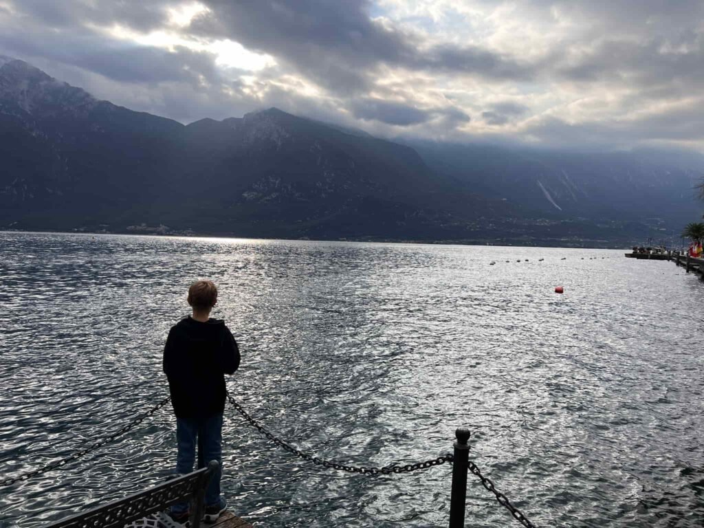 A boy staring at the beautiful view of Lake Garda on a sunset.