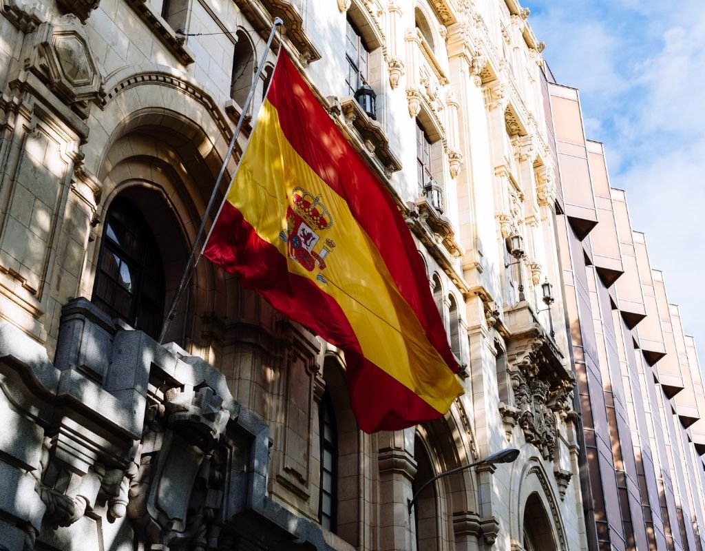 The Spanish flag flies on a historic building, blending past and present. Getting Spanish citizenship involves a commitment to the nation’s history and culture over time.