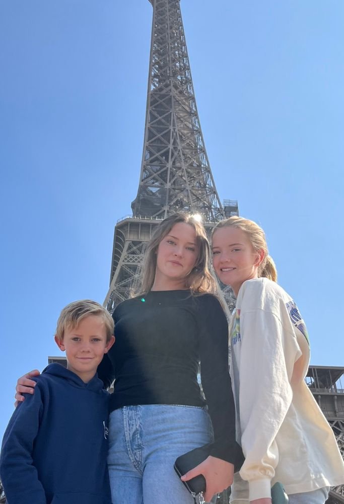 Colleen's three children smiling with the Eiffel Tower in the background, enjoying a sunny day in Paris. Having children in France implies childcare, which is very expensive, one of the bad things about living in France.