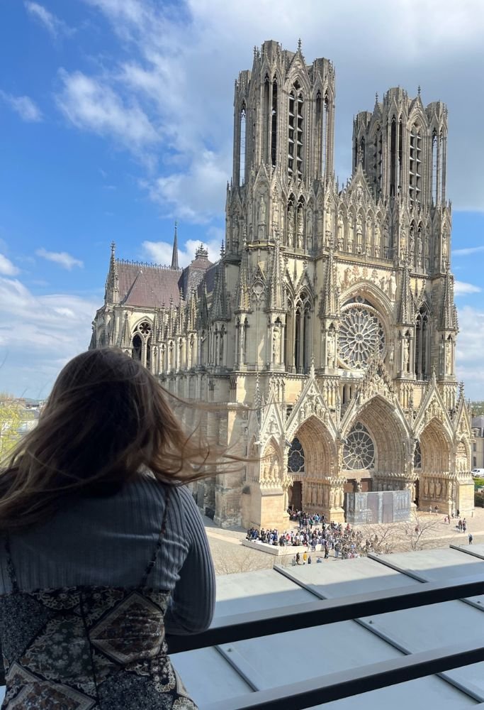 A view of Reims Cathedral in France, seen from a modern balcony, highlighting its intricate Gothic architecture with Colleen admiring the view.