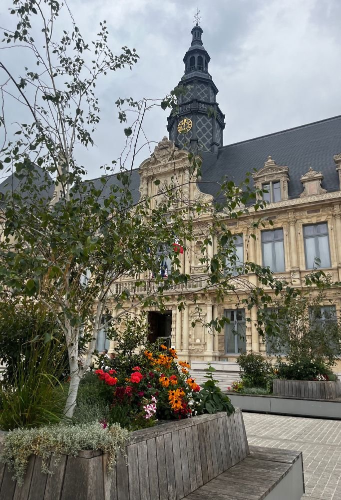 A detailed shot of a historical building with an ornate clock tower, surrounded by colorful flower beds and lush greenery. For Americans living in France, the architectural beauty often feels like stepping back in time.