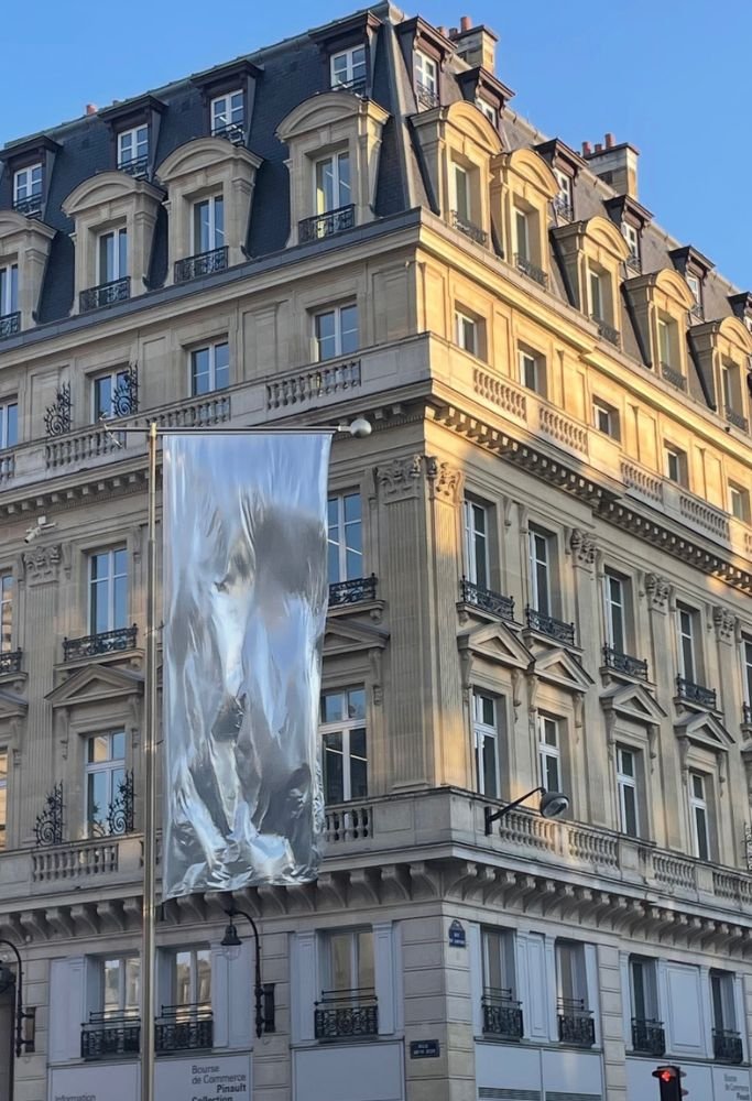 A grand Haussmann-style building in Paris, its golden light reflecting against the evening sky, with a contemporary silver flag waving in the foreground, showcasing the blend of history and modernity.