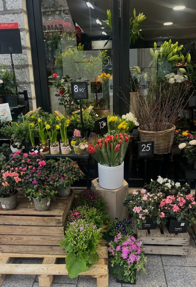 A quaint French flower shop with vibrant blooms and price tags, set on wooden crates.