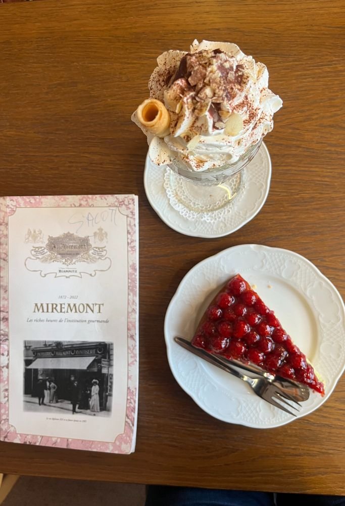 A creamy dessert topped with whipped cream and almonds, alongside a slice of raspberry tart on a plate, served at a café in France.