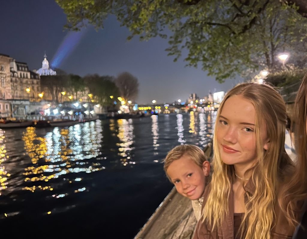 Children enjoying a peaceful evening by the Seine River, with the city's lights reflecting on the water.