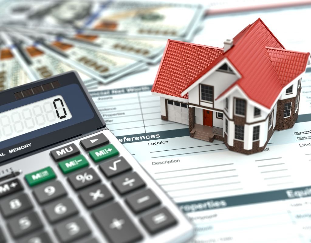 A small model house with a red roof sits on top of financial documents, next to a calculator and dollar bills, representing budgeting and planning required when buying a home in Mexico.