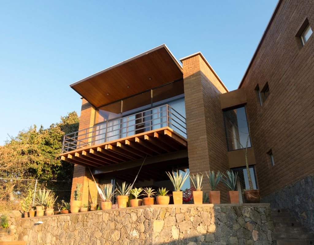 A modern house with a wooden balcony, large glass windows, and potted plants, illustrating contemporary design options available in Mexico.