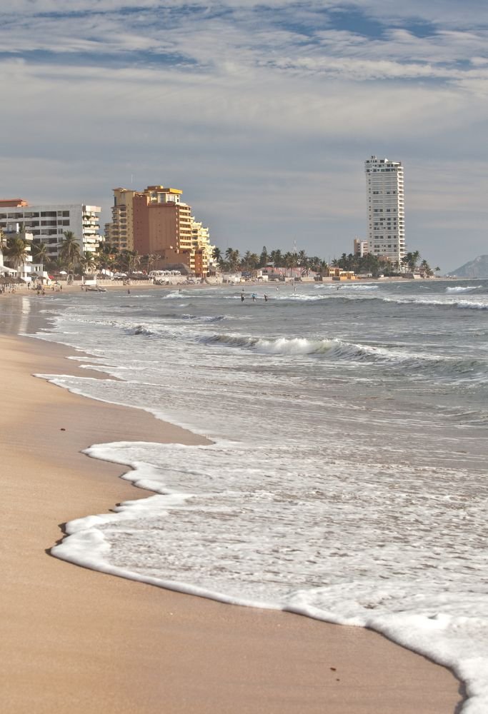 A scenic beachfront with golden sand and modern high-rise buildings, reflecting the blend of nature and urban life in Mexico.