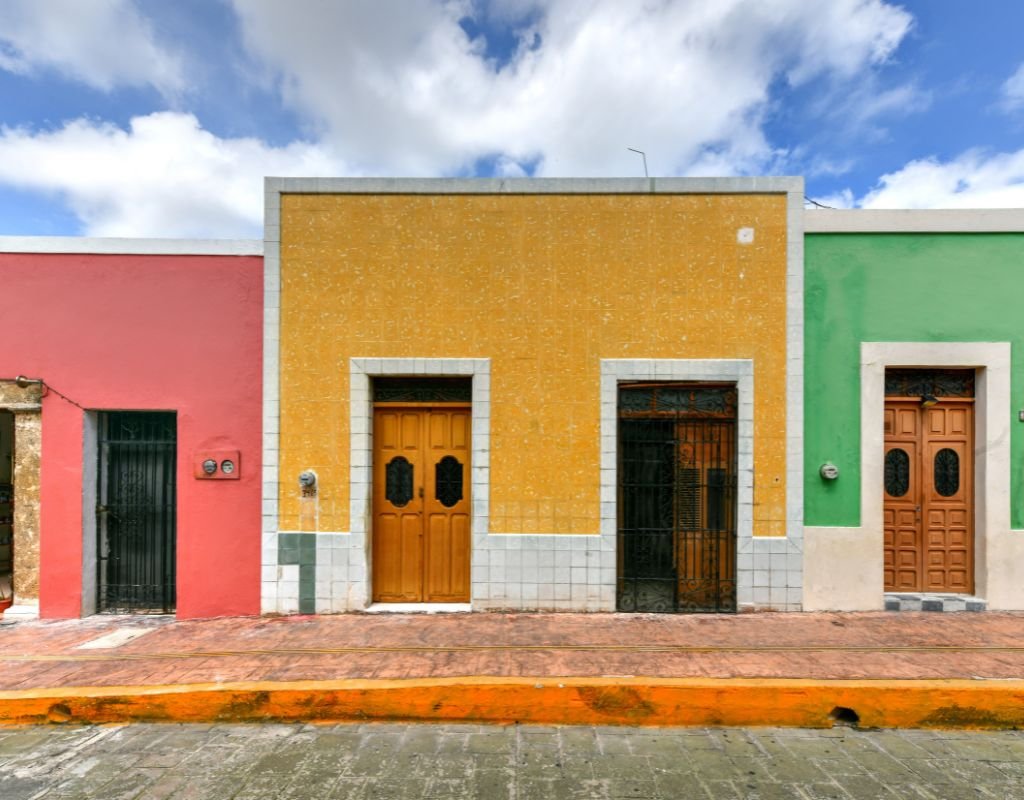 A row of colorful colonial-style houses in pink, yellow, and green, representing the vibrant and diverse architecture that attracts people to Mexico.