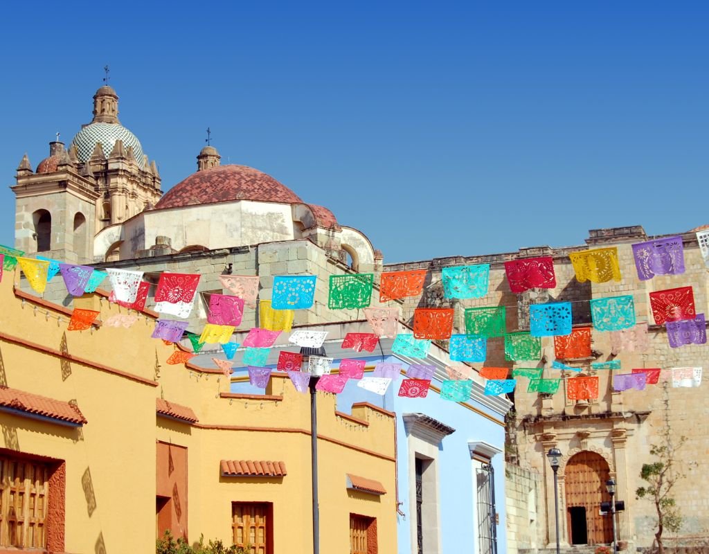 A festive display of colorful flags strung across a street with charming colonial architecture, highlighting the lively spirit of Mexican towns.