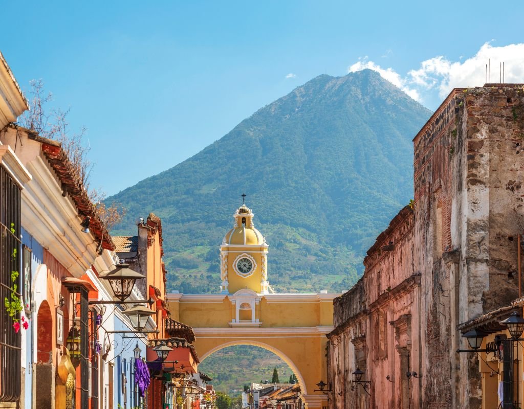 A cobblestone street leads to the iconic yellow Santa Catalina Arch in Antigua, Guatemala, with a majestic volcano rising in the background—one of the top countries Americans can move to for colonial charm and natural beauty.