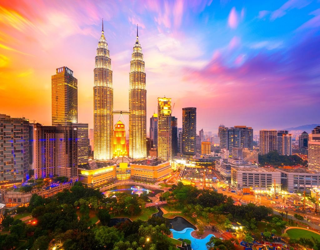 A glowing city skyline at dusk with the Petronas Towers standing tall in the heart of Kuala Lumpur, surrounded by modern skyscrapers and illuminated streets.